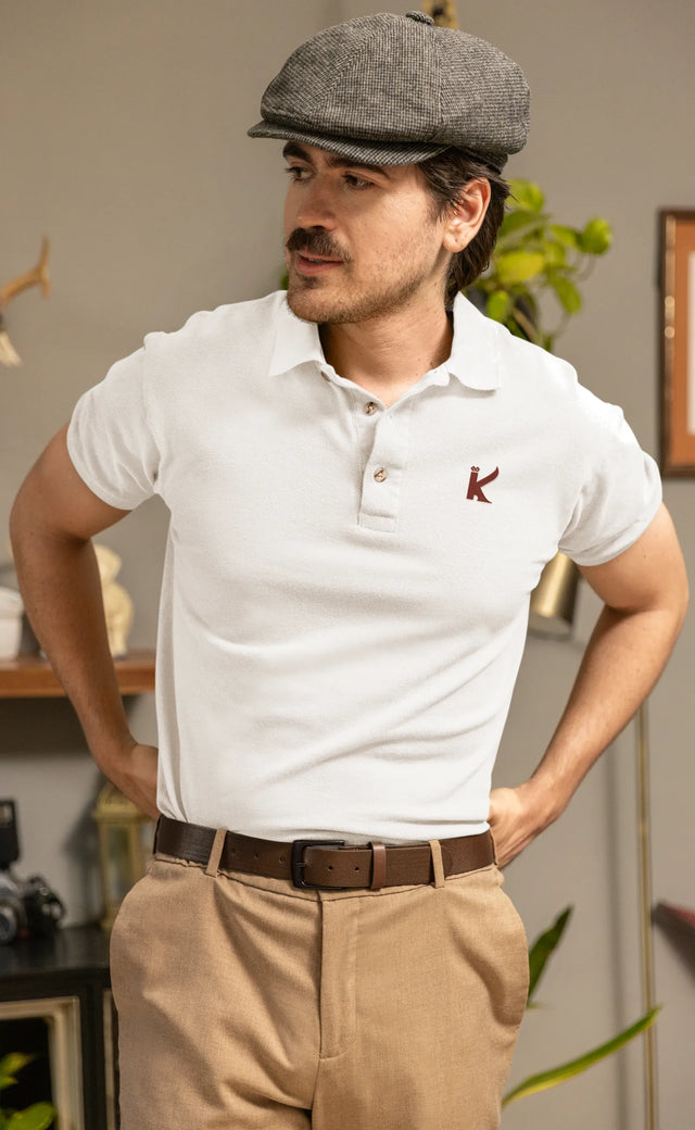 Man wearing a white polo shirt with a logo and beige pants indoors.