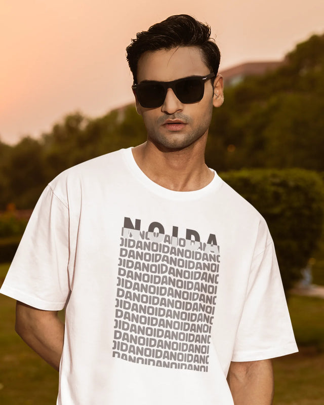 Man wearing a white t-shirt with text, standing outdoors with trees in the background