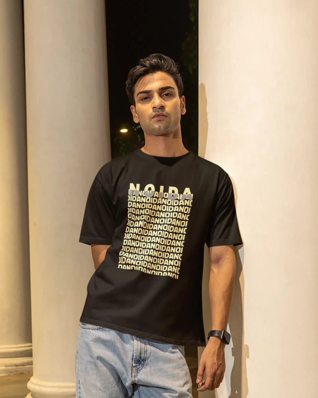Person wearing a black t-shirt with text standing against a light-colored wall.