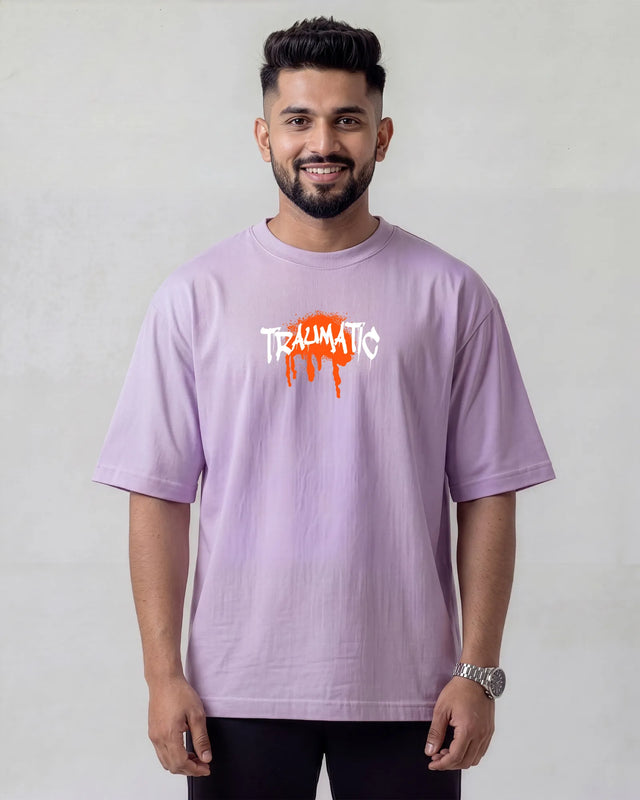 Man wearing a light lavender t-shirt with 'TRAUMATIC' print on a plain background