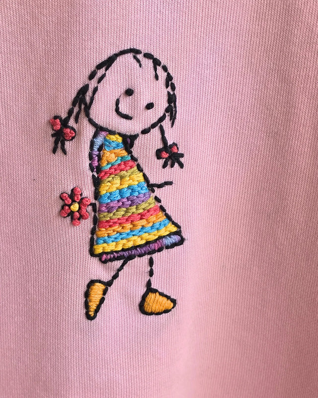 Embroidered design of a girl in a colorful dress on a Baby Pink French Terry background