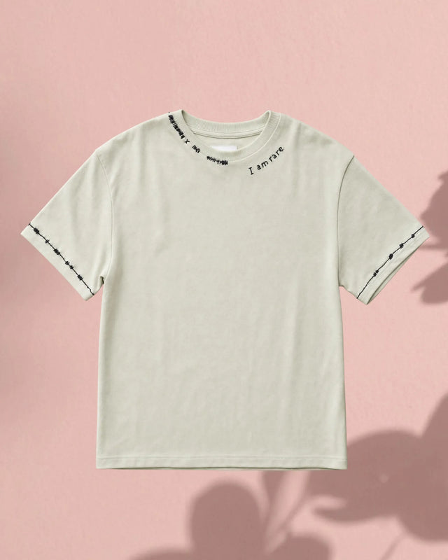 Light gray t-shirt with text on sleeves against a pink background
