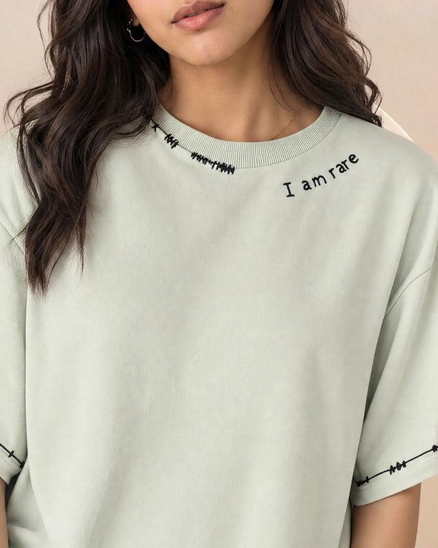 Person wearing a light green t-shirt with 'I am rare' text on a neutral background