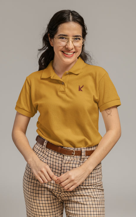 Woman wearing a mustard yellow polo shirt with a logo, standing indoors.