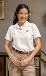 Woman wearing a white polo shirt with a logo and plaid pants indoors.