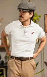 Man wearing a white polo shirt with a logo and beige pants indoors.