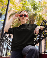 woman wearing a black t-shirt and red sunglasses sitting outdoors.