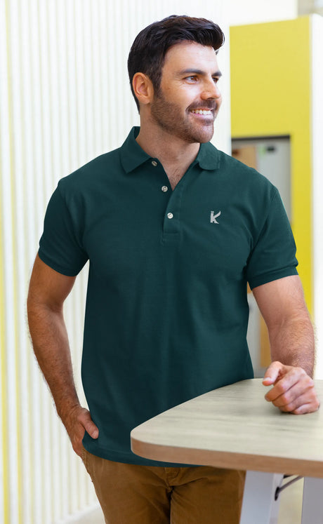 Man wearing a petrol blue polo shirt with a logo, standing indoors.