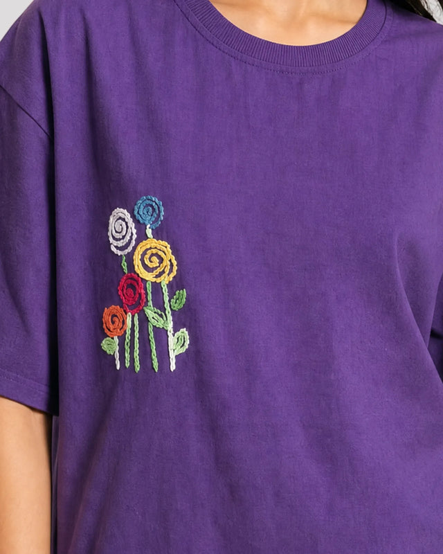 Purple t-shirt with embroidered colorful flowers on a plain background