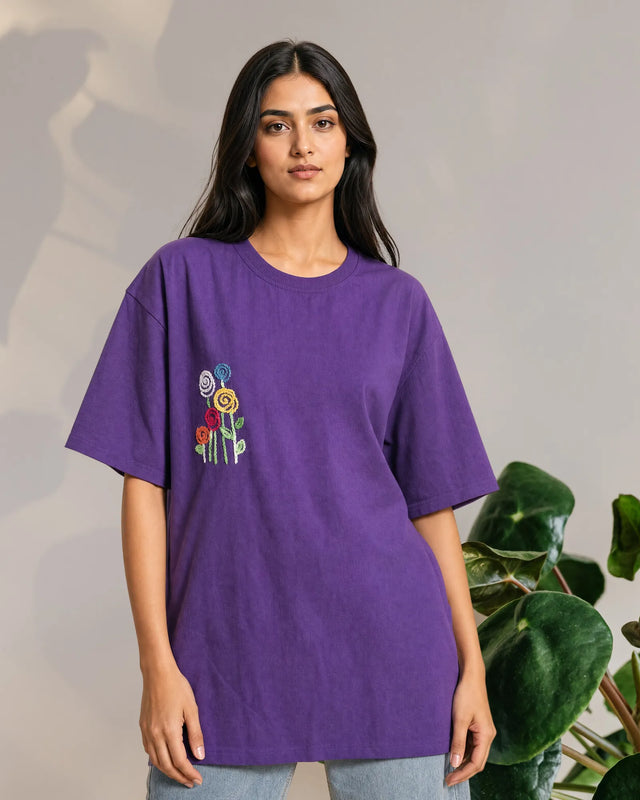 Woman wearing a purple t-shirt with colorful flower designs on a neutral background
