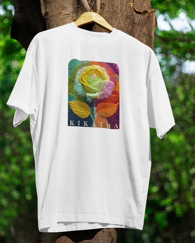 White t-shirt with a colorful rose design and 'Kikatra' branding on a hanger against a natural background.