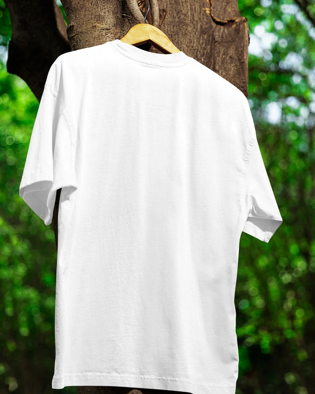 White t-shirt on a hanger against a natural background with green foliage.