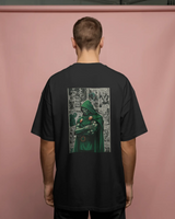 Person wearing a black t-shirt with a green character graphic on the back against a pink background