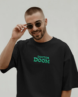 Man wearing a black t-shirt with 'Doctor Doom' text, holding sunglasses, on a plain background