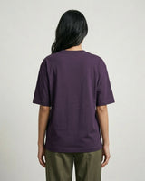 Person wearing a purple t-shirt and green pants on a plain background
