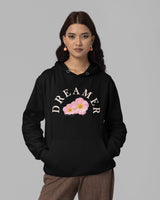 Woman wearing a black hoodie with 'DREAMER' and floral design on a gray background