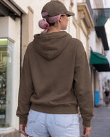 Person wearing a brown hoodie and cap, walking on a street.