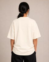 Person wearing a off-white t-shirt and black pants against a beige background