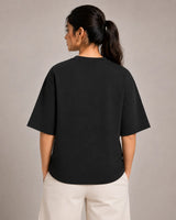 Person wearing a black t-shirt and beige pants against a plain background
