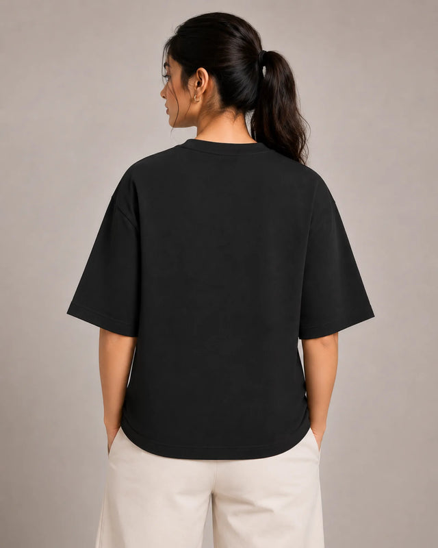 Person wearing a black t-shirt and beige pants against a plain background