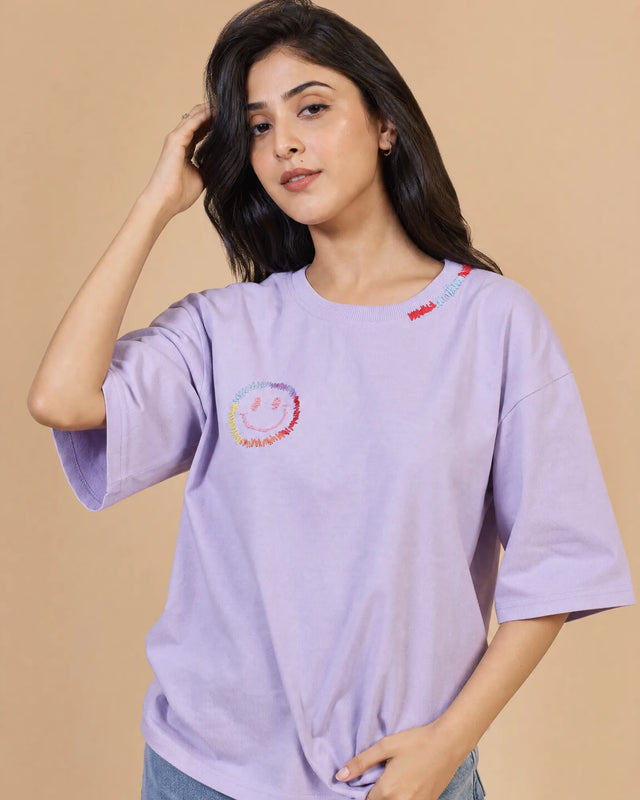 Woman wearing a light lavender t-shirt with a colorful logo on a beige background