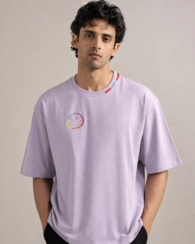 Man wearing a light lavender t-shirt with a colorful logo on a plain background