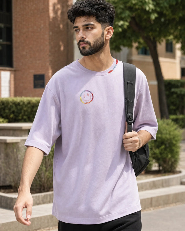 Man wearing a light lavender t-shirt with a smiley, walking outdoors.