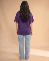 Person wearing a purple t-shirt with yellow trim and blue jeans on a beige background