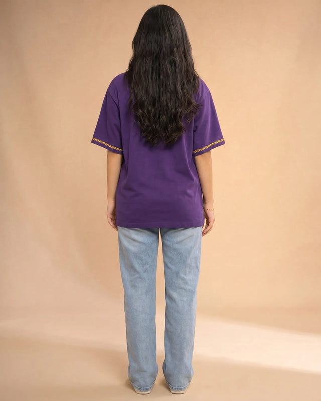 Person wearing a purple t-shirt with yellow trim and blue jeans on a beige background