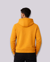 Person wearing a mustard yellow hoodie from behind on a light gray background