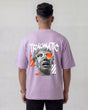 Person wearing a lavender t-shirt with graphic design and text on the back, against a plain background