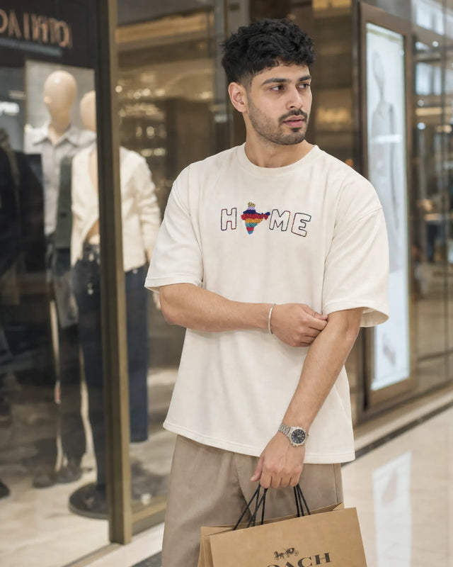 Man wearing a white t-shirt with 'HOME' printed on it, standing in front of a store window.