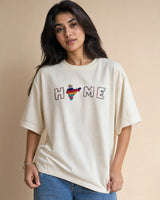 Woman wearing a white t-shirt with a colorful 'HOME' graphic on a beige background