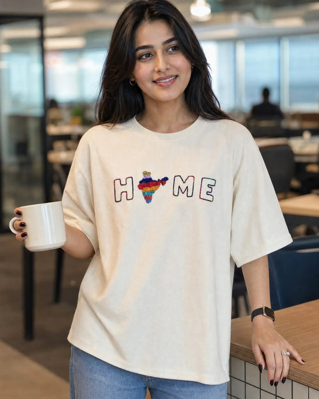 Woman wearing a t-shirt with 'HOME' and a rainbow heart design, holding a mug in an office setting.