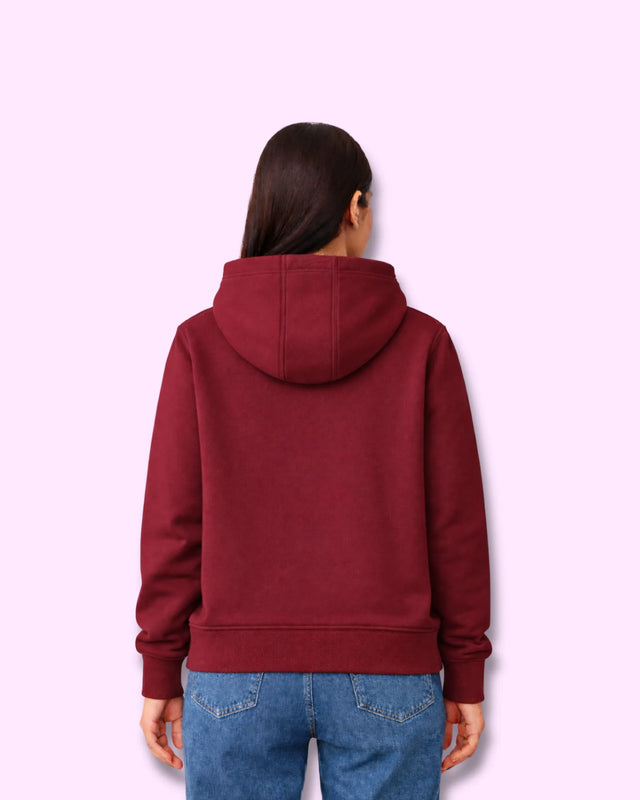 Woman wearing a maroon hoodie and blue jeans on a light purple background with back view
