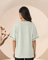 Person wearing a light green t-shirt with black trim on a beige background