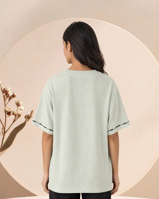 Person wearing a light green t-shirt with black trim on a beige background