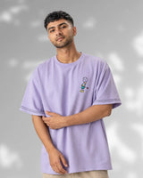 Man wearing a light purple t-shirt with a small graphic on a gray background