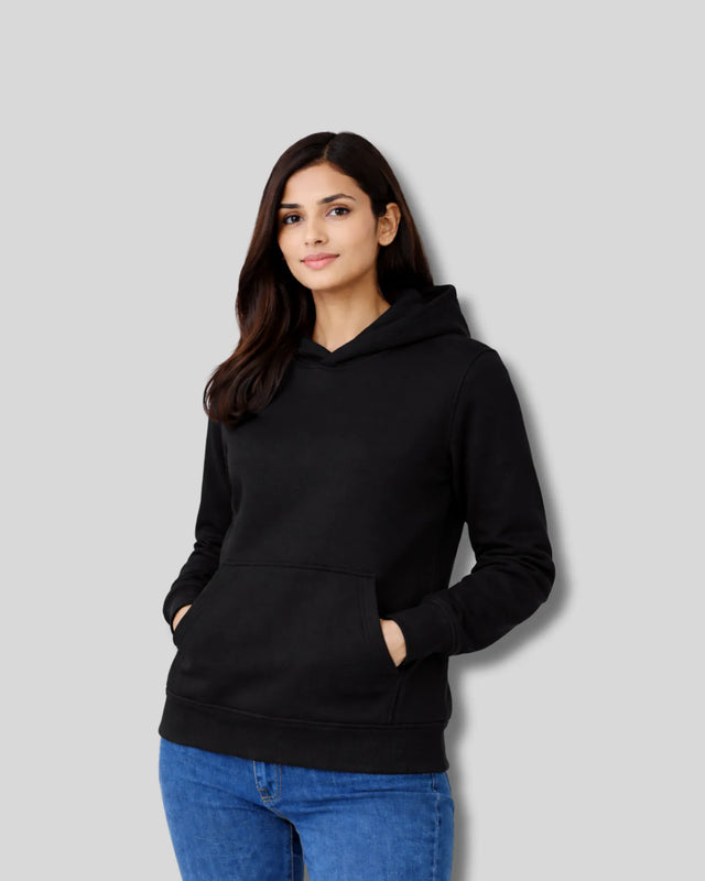 Woman wearing a black hoodie and blue jeans against a gray background